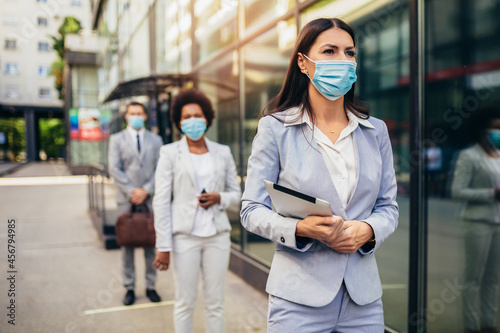 Business people with protectiveface mask waiting in line on a safe distance during COVID-19 epidemic. © Mediteraneo