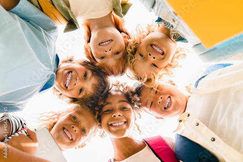 Low angle view of a group of mixed-race multi-ethnic classmates schoolchildren kids standing in round ring together smiling before classes lessons at school. photo