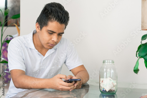 man doing online shopping, bad financial situation, guy texting on his mobile phone, banknotes on the table, bankrupt young man, spending his savings. economic concept