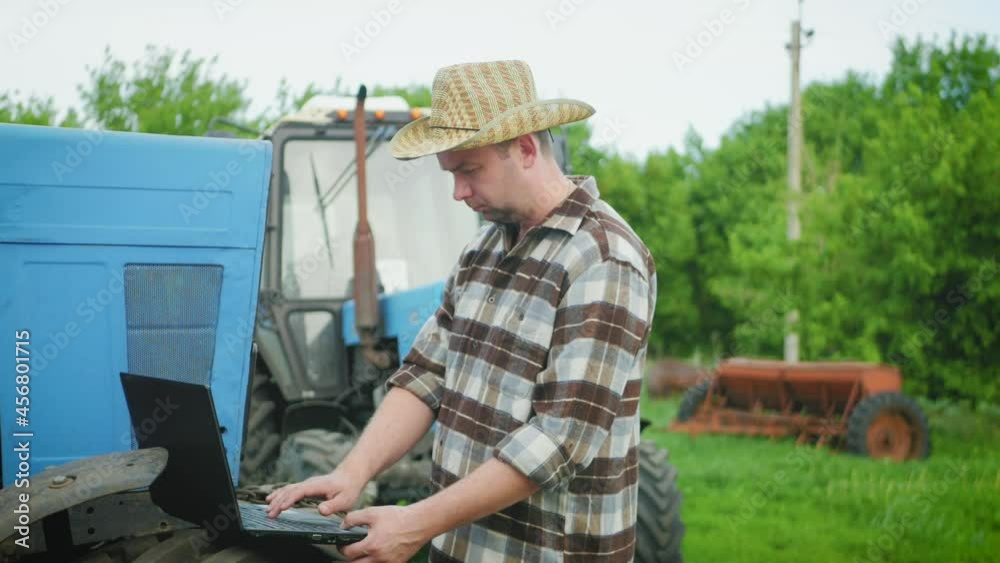 Smart farming. Applying modern technology in agricultural activity. Young landowner with computer work. Man technical worker with laptop works next to the tractor. Concept modern technology. Smart farming. Applying modern technology in agricultural activity. Young landowner with computer work. Man technical worker with laptop works next to the tractor. Concept modern technology.