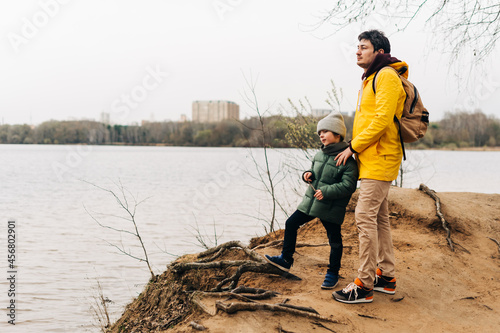 Father and son stand on the shore of the lake and hold hands. Happy family with child kid boy playing and having fun outdoors over autumn park background