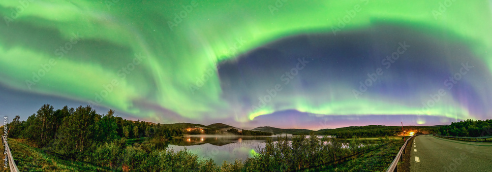 Wide Panorama Aurora borealis, Northern green lights with lot stars in the night sky over mountain lake, mirrored reflection in water, night mist. Night road, Joesjo, Northern Mountains, Sweden