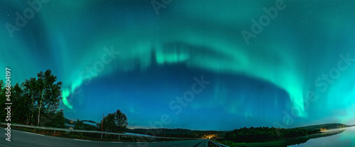 Panoramic Aurora borealis, Northern green lights with lot stars in the night sky over mountain road in mountains, mirrored reflection in water, night mist. Joesjo, Northern Sweden