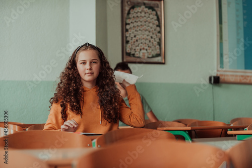 A nervous little girl throws a mask against corona virus protection while sitting at a school desk.New normal. Education during the Covid-19 pandemic. Selective focus.