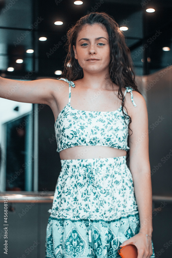 Muchacha joven de pelo rizado oscuro posando con una sonrisa en el ascensor de una empresa para acceder a la siguiente planta Muchacha joven de pelo rizado oscuro posando con una sonrisa en el ascensor de una empresa para acceder a la siguiente planta