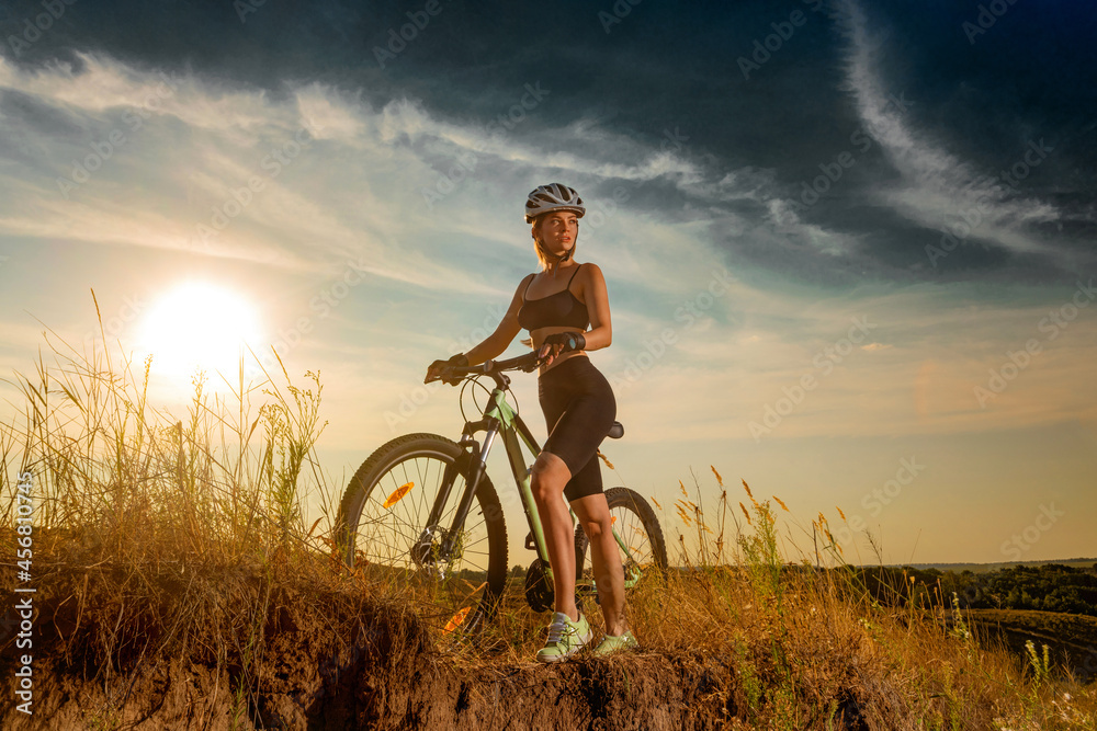 Biker-girl at the sunset with mountain bike. Woman with bicycle at sunrise on trail. Biker-girl at the sunset with mountain bike. Woman with bicycle at sunrise on trail.