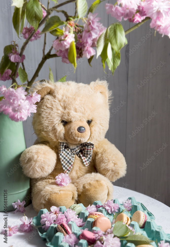 teddy bear sits on the table against the background of sakura and easter cookies