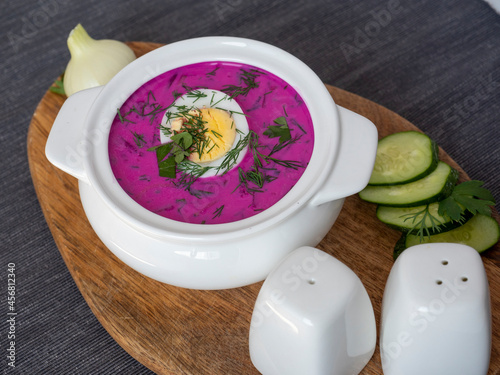 Close-up of cold chlodnik soup on a wooden board. Soup of Polish Belarusian and Russian cuisine made of beetroot and kefir, decorated with half an egg. Healthy food. photo