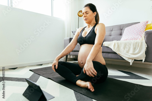 Pregnant woman exercising at home. Pregnant woman wearing gym clothes doing yoga or meditating in her living room.