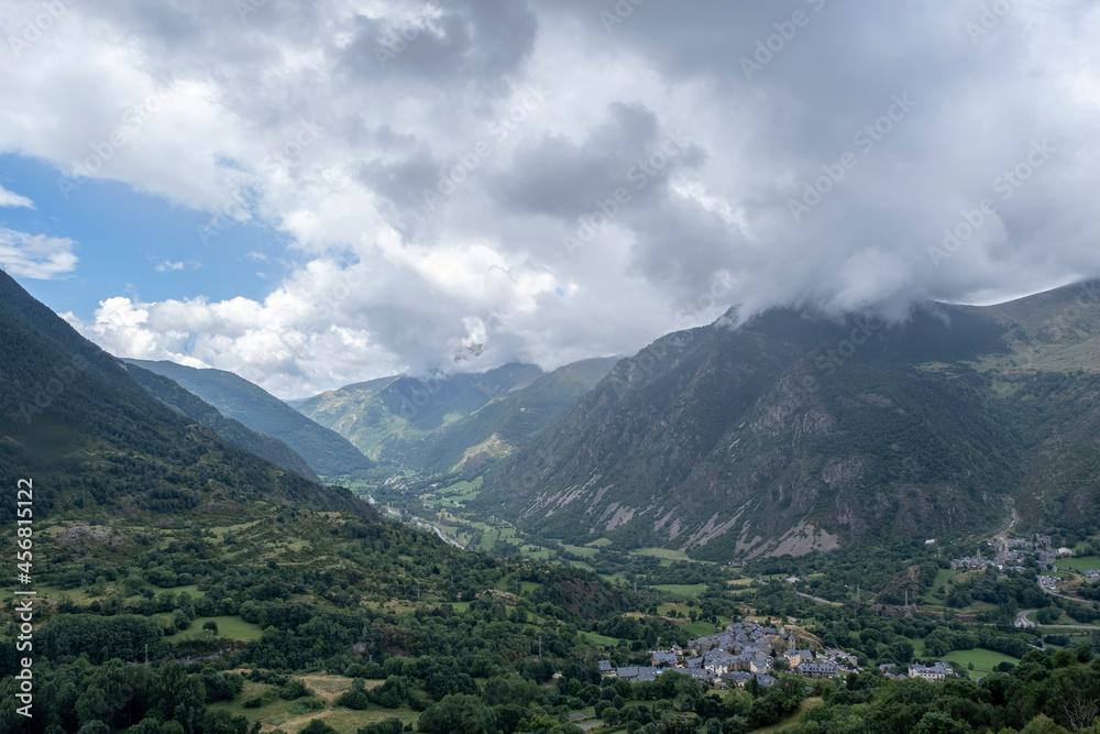 View of the Boi Tahull valley with the village of Boi and Erill la Vall with the mountains of the Lleida Pyrenees in the background on a cloudy summer day