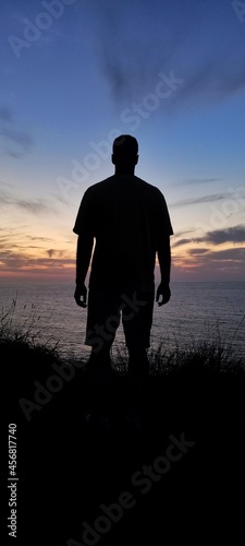 A silhouette of a man in the coast with the ocean and the sunset in the background