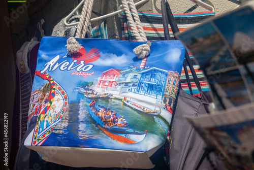 Aveiro, Portugal - June 11, 2021: Souvenir colorful bag in the street shop with a landscape of Aveiro canal and a gondola colorful boat on it and postcards in the foreground, Text Aveiro city Portugal