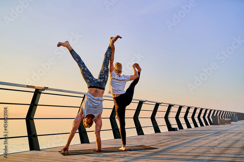 Couple practicing acrobatic handstand yoga together on nature outdoors at sea.