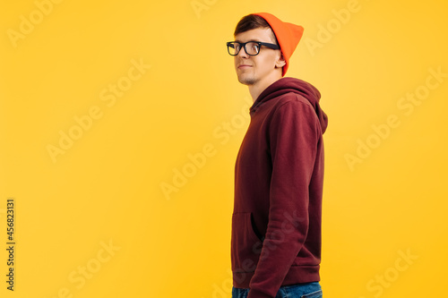 portrait of a handsome guy in an orange hat, red sweater and glasses, on a yellow background, smiling broadly
