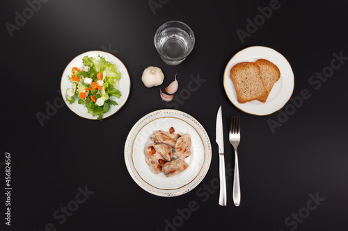 top view of table set with chicken dishes, salad, wholemeal bread, water and garlic. Black background with copy space.