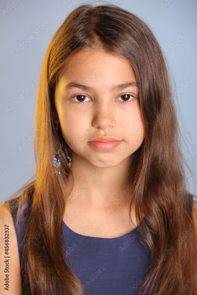Close-up portrait of a beautiful dark-haired teenage girl 12 years old in a blue dress. She looks carefully eye to eye. Close-up portrait of a beautiful dark-haired teenage girl 12 years old in a blue dress. She looks carefully eye to eye.