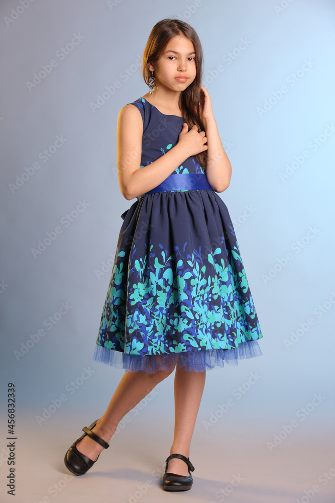 Portrait in full growth pretty slim dark-haired teenage girl 12 years old in a blue dress.
