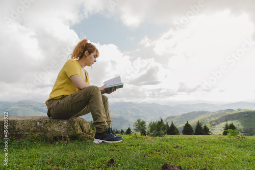 Caucasian female in a yellow t-shirt reading a book in a forest