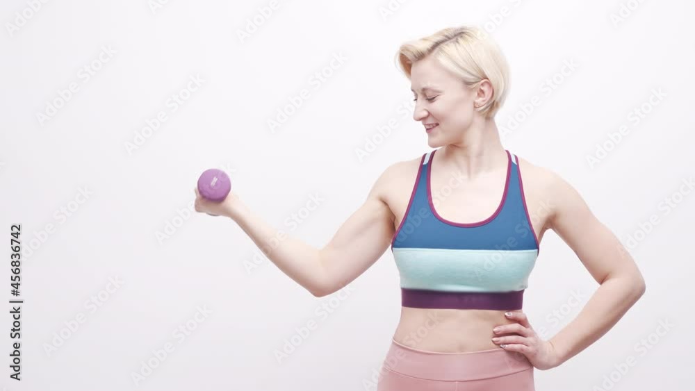 Young blonde woman lifting a dumbbell with a smile on her face Young blonde woman lifting a dumbbell with a smile on her face