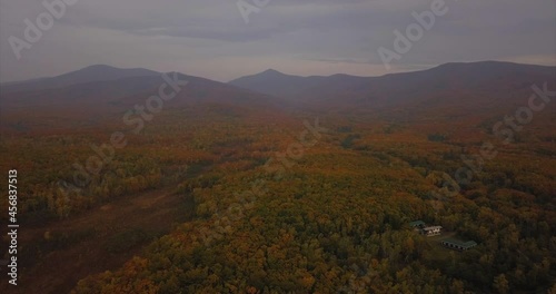 Aerial view of amazing autumn forest, silhouettes of mountaisn on the background and a house in the middle of the wood. Russian taiga. Far East photo