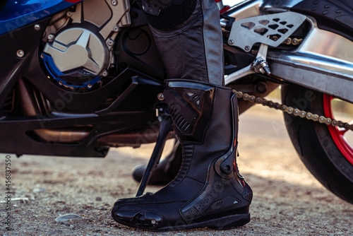 Closeup shot of a male's boot in front of a motorcycle