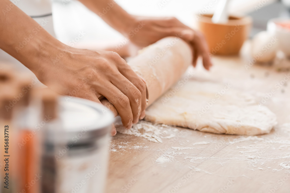 Young woman rolling out dough in kitchen, closeup