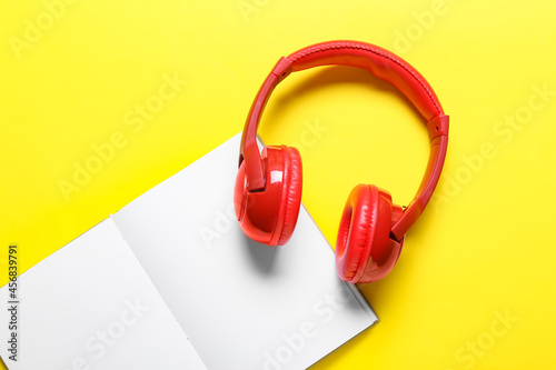 Modern headphones with book on color background