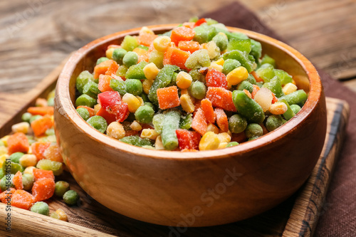Bowl with mix of frozen vegetables on wooden background, closeup