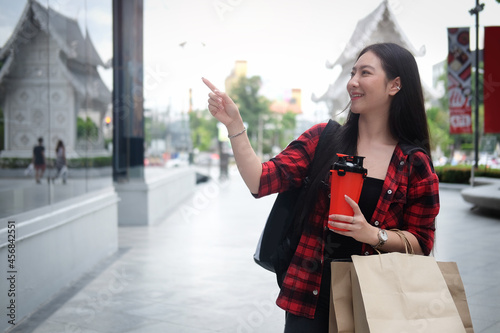 Smiling young woman holding shopping bags and coffee cup walking on the city street.