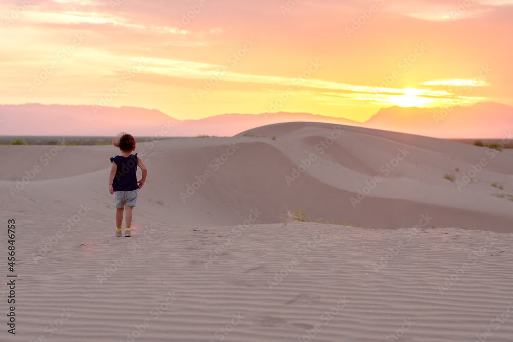 Unrecognizable child walking in a desert at sunrise
