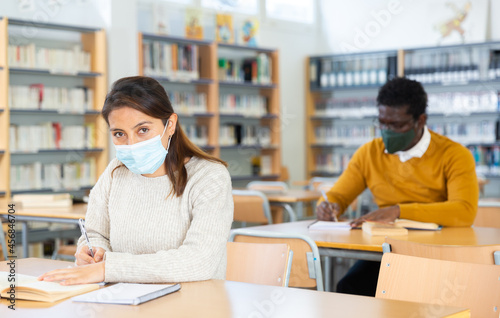 Adult female student in face mask working in library, concept of adult education during coronavirus pandemic