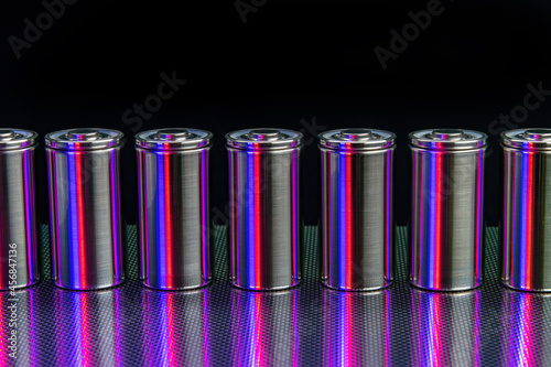 A pack of new modern high-capacity lithium-ion cells. A prototype of new batteries on a steel surface illuminated with red and blue light on a black background