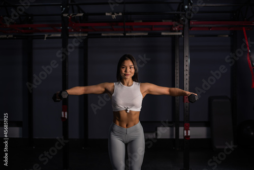 Asian woman doing exercises with dumbbells in the gym.