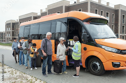 Female transportation supervisor in green vest standing at open bus door and checking tickets of passengers