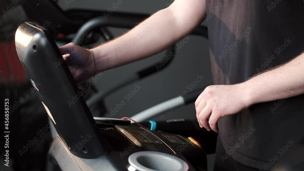 Handsome sports man sets up a treadmill Handsome sports man sets up a treadmill