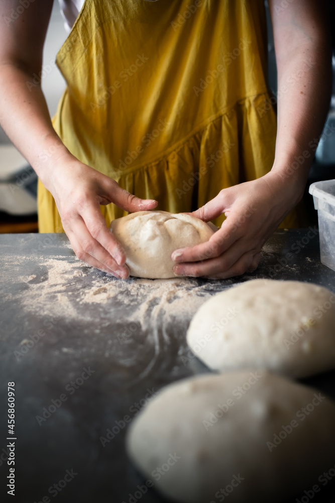 Fototapeta premium Woman baker forms bread on a steel table in a bakery