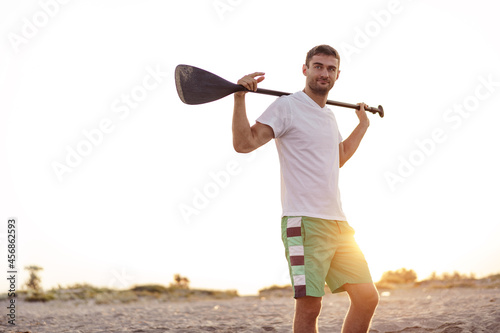 Young fit man standing on the beach and holding paddle