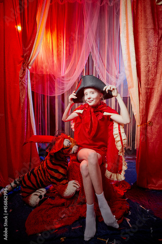Young teenager girl during a stylized theatrical circus photo shoot in a beautiful red location. Young model posing on stage with curtain
