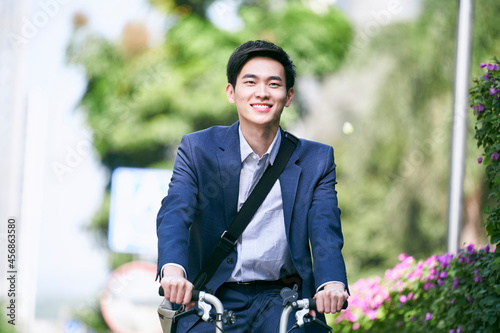 Fotografija young asian businessman commuting by bike on street in modern city