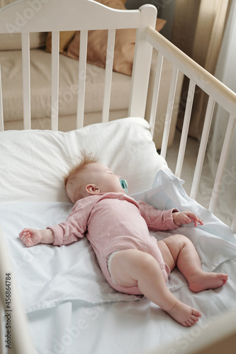 Adorable baby girl with pacifier in mouth sleeping peacefully in cradle