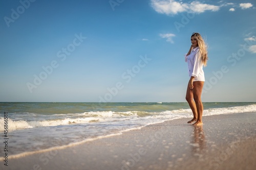 A tanned girl in a blue swimsuit and a light shirt enjoys the summer at the seaside