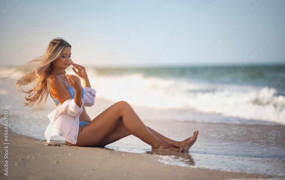 A girl in a bluish swimsuit and shirt sits near the water edge and peers into the horizon A girl in a bluish swimsuit and shirt sits near the water edge and peers into the horizon