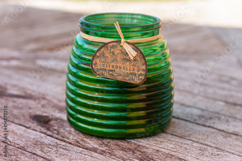 Scented green citronella glass candle holder used as a mosquito repellent standing on a wooden table top. Lemongrass green candles to prevent mosquitoes prick and to keep them away on a summer evening