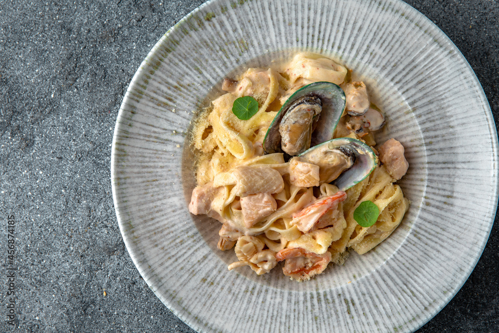 Pasta in a creamy sauce with seafood: mussels, shrimps, salmon and octopus. Ready menu for the restaurant. Neutral gray blue textured background Pasta in a creamy sauce with seafood: mussels, shrimps, salmon and octopus. Ready menu for the restaurant. Neutral gray blue textured background