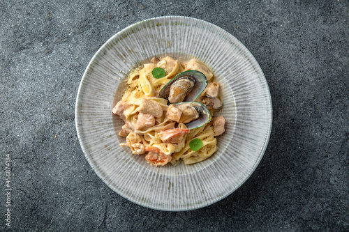 Pasta in a creamy sauce with seafood: mussels, shrimps, salmon and octopus. Ready menu for the restaurant. Neutral gray blue textured background