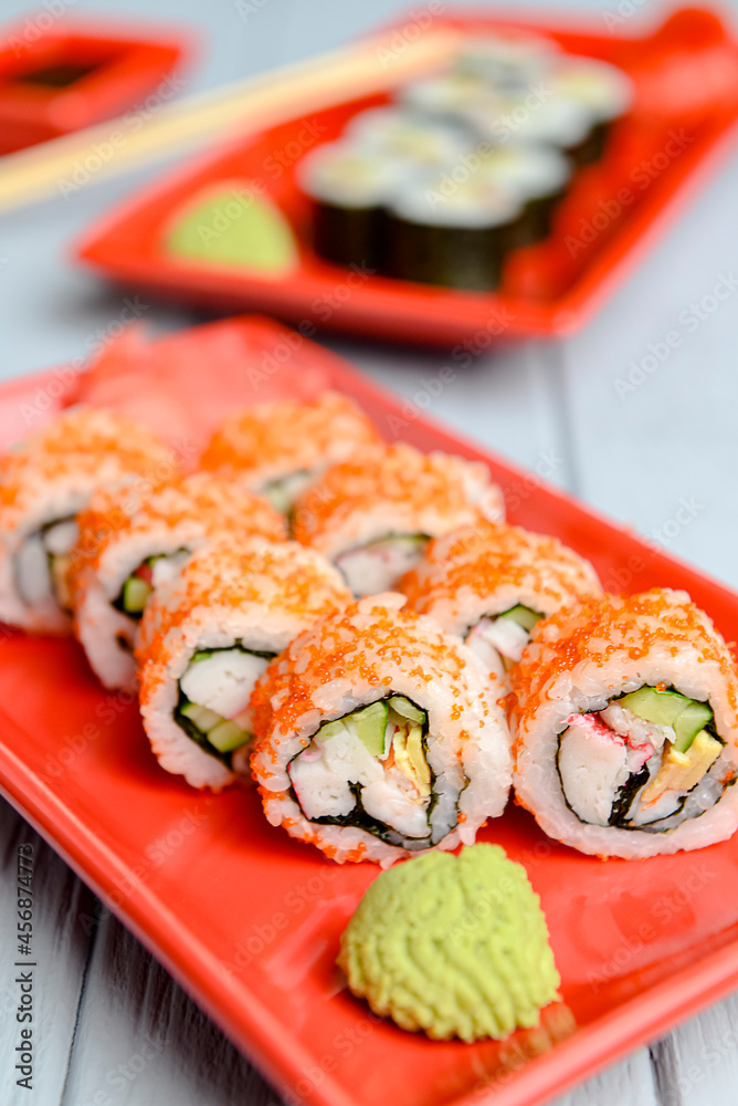 California sushi rolls served on a red plate over light wooden background. Close up, selective focus on sushi. California sushi rolls served on a red plate over light wooden background. Close up, selective focus on sushi.