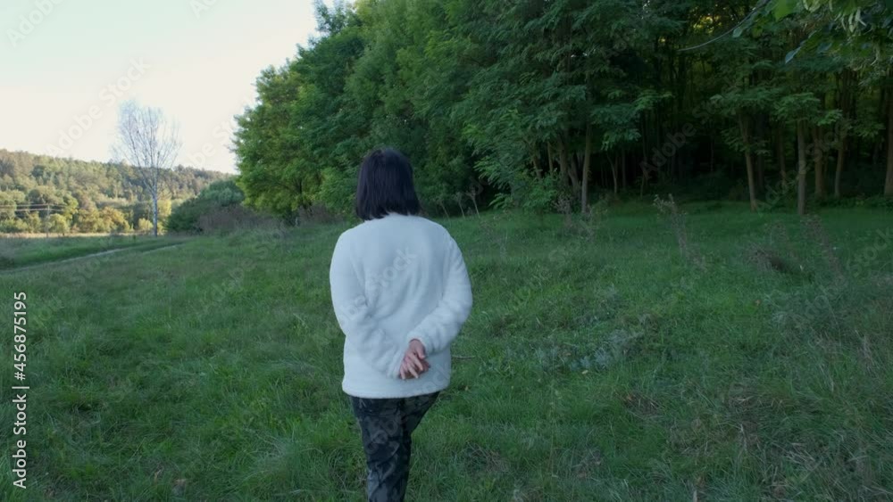 Woman walking in the green forest in sunny day. Back view, 4K