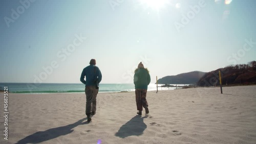 Backs of the young couple walking along the epmty sandy beach. Wonderful sunny autumn day. Okunevaya bay of sea of Japan. Russia, Nakhodka photo