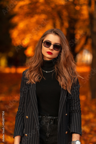 Stylish beauty business woman with red lips in fashionable clothes with vintage sunglasses walks in the park with colored orange foliage