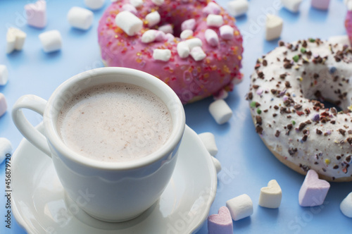Pink and white donuts, cup of cocoa marshmallows in the shape of heart on blue background